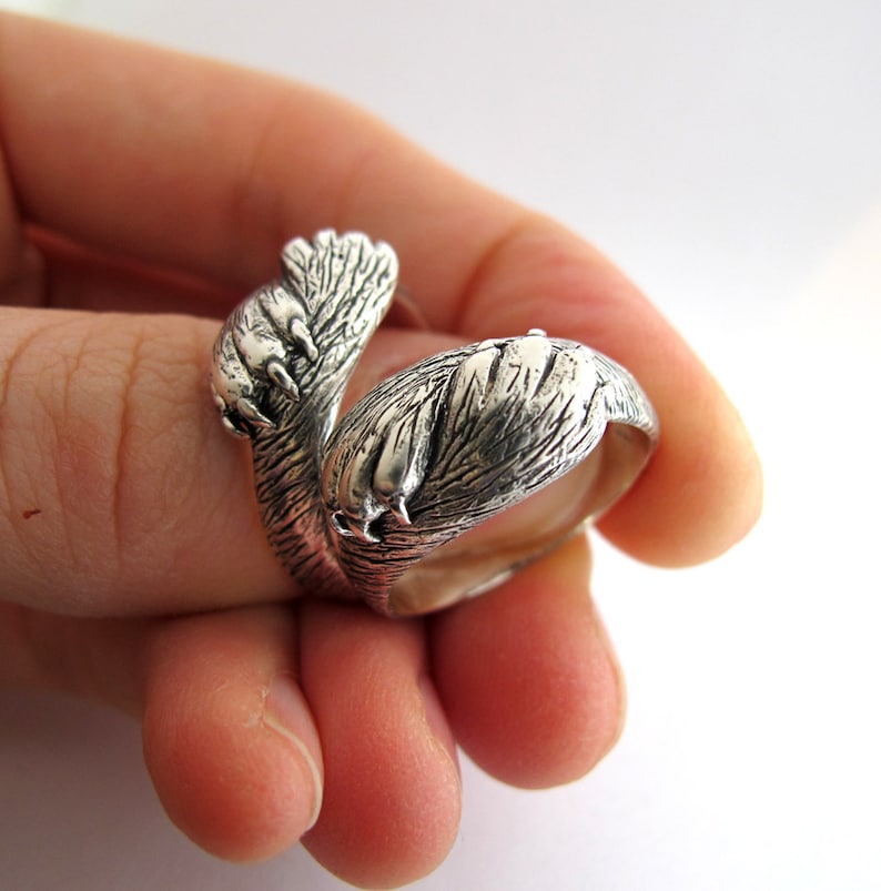 May include: A silver ring shaped like a pair of animal paws wrapped around each other. The ring is detailed with textured fur and claws.