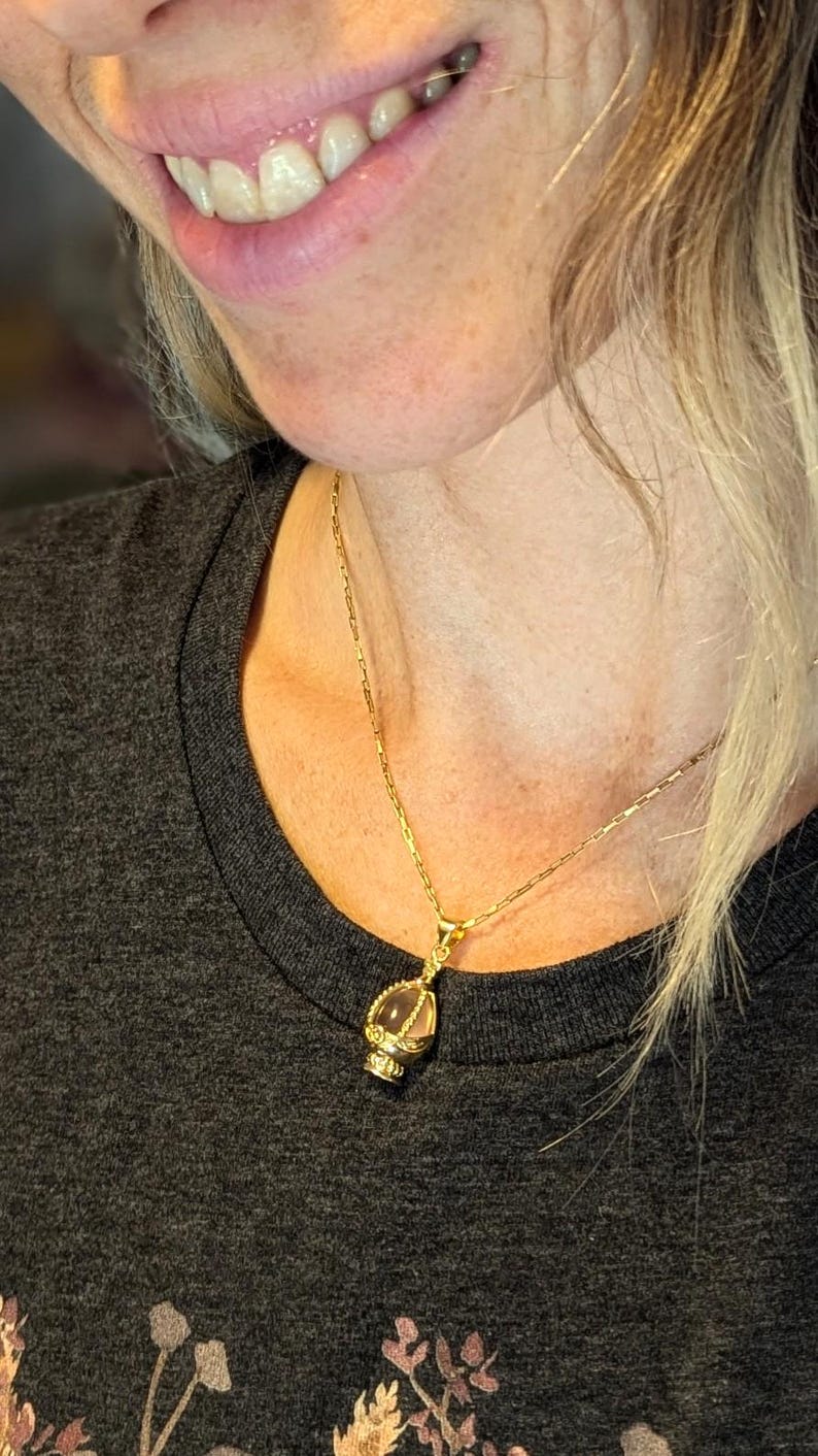 May include: A gold chain necklace with a clear crystal pendant in a gold cage design.