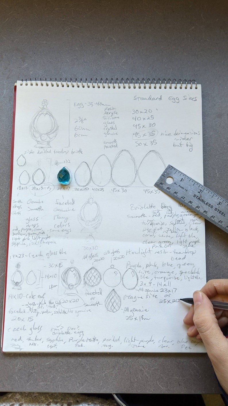 May include: Handwritten notes on a notebook page about egg sizes and types of glass beads. The notes include measurements in inches and centimeters, colors, and descriptions of the beads. The page also includes a ruler and a drawing of a teardrop-shaped briolette bead.