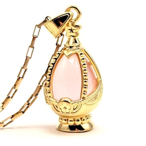 May include: A gold pendant necklace with a pink gemstone in the center. The pendant is shaped like an egg and has intricate details.