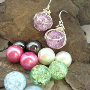 Pode incluir: Um par de brincos com contas de vidro roxo e verde, juntamente com uma variedade de outras contas em diferentes cores e materiais.