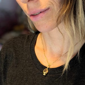 May include: A woman wearing a dark grey t-shirt with a floral print and a gold chain necklace with a small pendant.