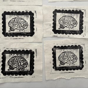 May include: Four fabric squares with a black and white brain print. Each brain image is framed within a black scalloped border. The fabric has a natural, off-white color.