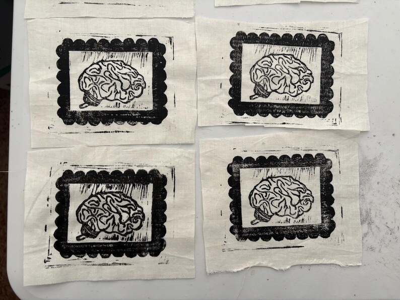 May include: Four fabric squares with a black and white brain print. Each brain image is framed within a black scalloped border. The fabric has a natural, off-white color.