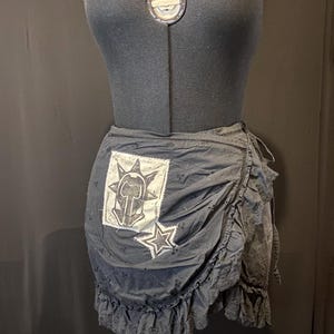 May include: A black wrap skirt with a ruffled hem. The skirt has a white patch with a black star and a black and white graphic design.