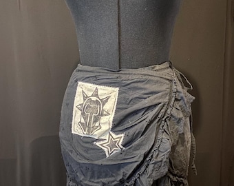 Pode incluir: Uma saia preta de amarrar com uma bainha franjada. A saia tem um remendo branco com uma estrela preta e um design gráfico preto e branco.