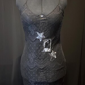 May include: Black lace slip dress with a silver star and a silver rectangle design on the front.