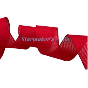 May include: A vibrant red ribbon with a textured, woven mesh finish, displayed in a series of elegant, flowing loops. The text Starmaker's Attic is printed in a light blue font across the center of the ribbon, which features a consistent, open-weave pattern throughout its length.