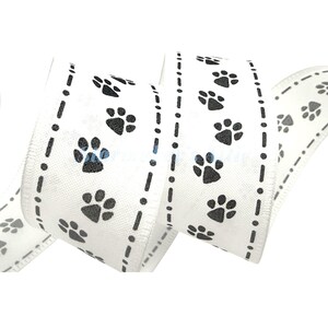 May include: White ribbon with a repeating pattern of black paw prints and dotted lines. The ribbon is curled, showing the pattern on both sides. A few paw prints have blue accents.