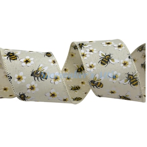 May include: A decorative ribbon with a repeating pattern of yellow and black bees and white flowers on a light beige background. The ribbon is curled and has a textured appearance, suitable for crafts and gift wrapping.