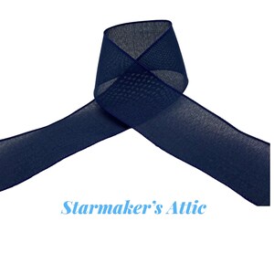 May include: Navy blue sheer ribbon with a textured weave. The ribbon is folded in half and has a slightly frayed edge.