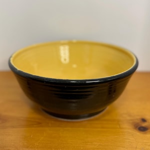 May include: A black bowl with a yellow interior. The bowl has a rounded shape and a smooth, glossy finish.