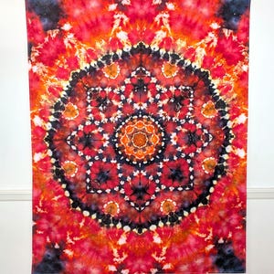 May include: A vibrant, tie-dye tapestry with a mandala design. The color palette includes shades of red, orange, black, and white, creating a striking visual effect. The circular pattern is centered and symmetrical, perfect for wall decor.