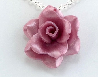 May include: A silver chain necklace with a pink rose pendant. The rose is made of a smooth, shiny material.