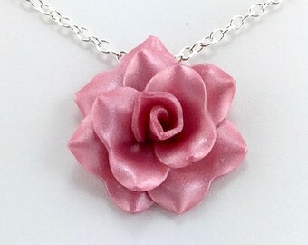 May include: A silver chain necklace with a pink rose pendant. The rose is made of a smooth, shiny material and has a realistic appearance.