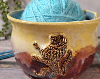 May include: Ceramic yarn bowl with a lion design in brown, yellow, and red glaze. A ball of light blue yarn is inside the bowl.