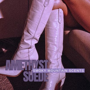 May include: A pair of light purple suede knee-high boots with a pointed toe and a high heel. The boots have a decorative strap near the top. The text "AMETHYST SUEDE - SMOKY MOUNTAIN SCENTS" is overlaid on the image.
