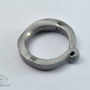 May include: A silver ring with a twisted design and a small gold dot on the side. The ring has a small hole on the side and is marked with the letter "F" and a symbol.