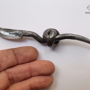 May include: A hand-forged metal knife with a knotted handle. The blade is curved and the handle is twisted into a knot.