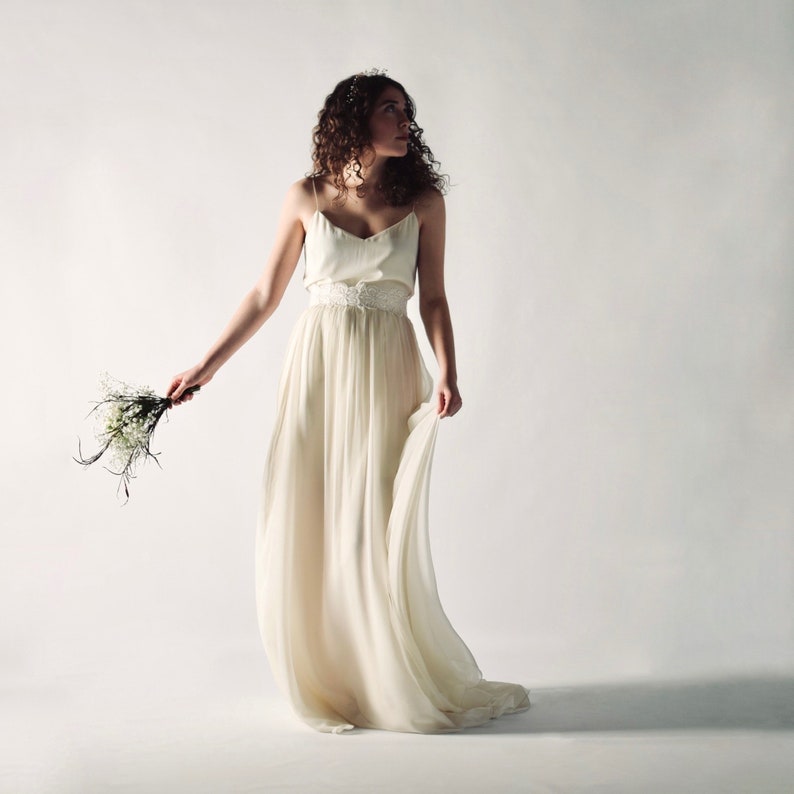 May include: A woman in a white wedding dress with a lace belt and a bouquet of white flowers.