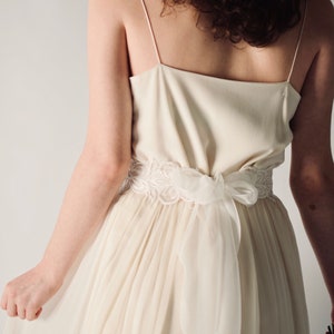 May include: A white wedding dress with a lace sash and a flowing skirt.