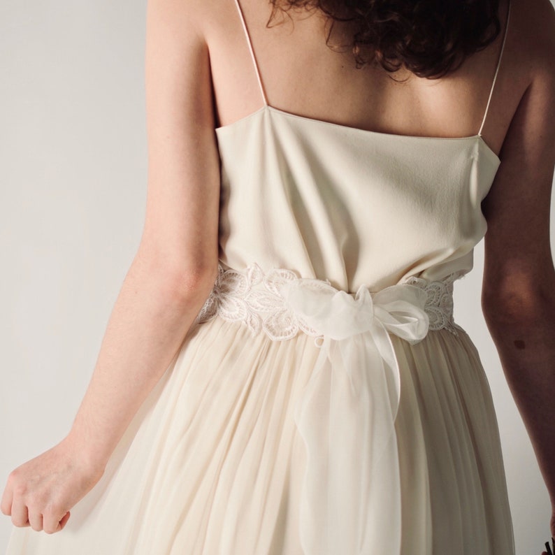 May include: A white wedding dress with a lace sash and a flowing skirt.