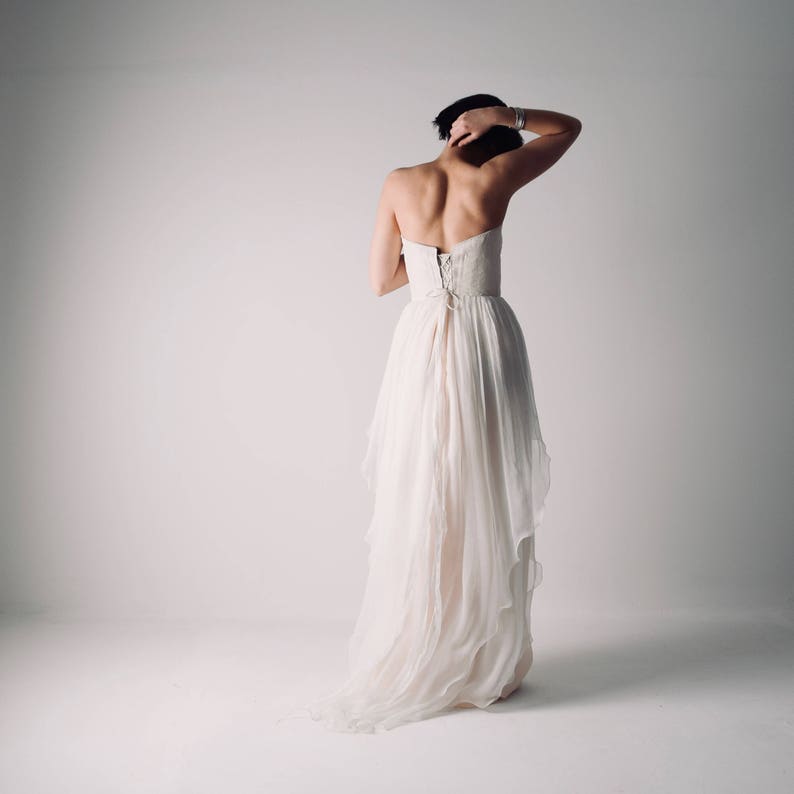 Op de afbeelding: Een witte strapless bruidsjurk met een vloeiende rok en een kanten lijfje. De jurk heeft een lange sleep en is gemaakt van een lichtgewicht stof.