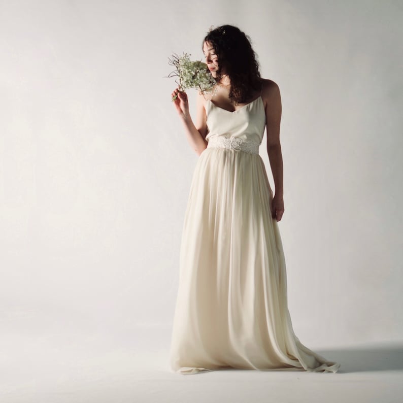 May include: A woman in a white wedding dress with a lace belt and a bouquet of white flowers.
