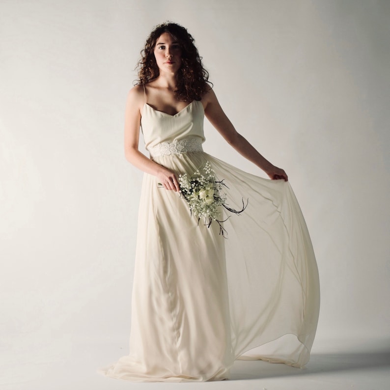 May include: A woman wearing a white wedding dress with a floral sash and a bouquet of white flowers.