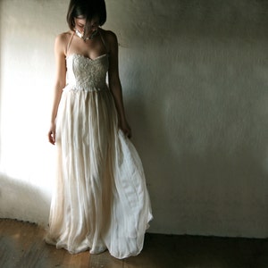 May include: A woman wearing a white, lace-trimmed, strapless gown with a flowing skirt. The gown is made of a sheer fabric and has a delicate, romantic look.