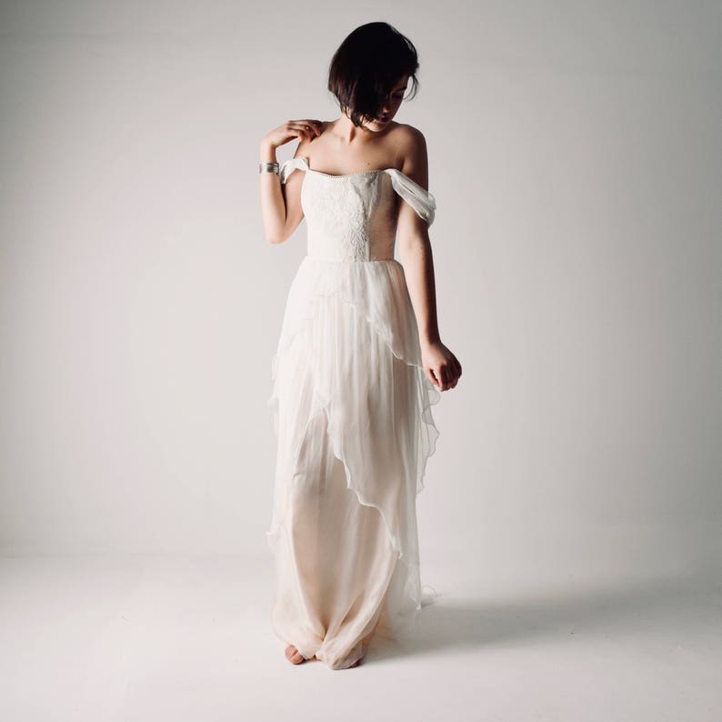 Op de afbeelding: Een witte, off-shoulder bruidsjurk met een gelaagde rok en een strak lijfje.