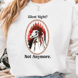 May include: White sweatshirt with the text "Silent Night? Not Anymore." The design features an oval graphic with a skeletal horse head and red accents. A Santa mug is held in the hand.