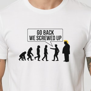 Puede incluir: Camiseta blanca con un gráfico negro que representa la evolución humana, culminando en una caricatura con pelo amarillo. Un bocadillo sobre la figura dice "GO BACK WE SCREWED UP."