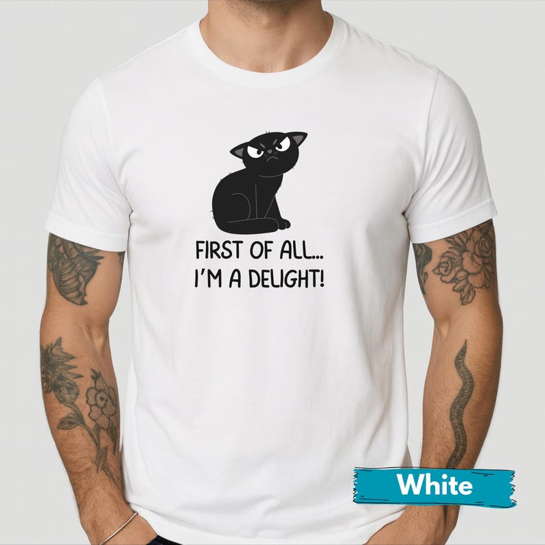 May include: White t-shirt featuring a black cartoon cat with an angry expression. The text "FIRST OF ALL... I'M A DELIGHT!" is printed below the cat. The shirt has short sleeves and a crew neck.