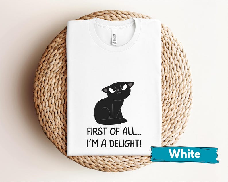 May include: White t-shirt featuring a cartoon black cat with an angry expression. The text "FIRST OF ALL... I'M A DELIGHT!" is printed below the cat. A teal banner at the bottom reads "White".