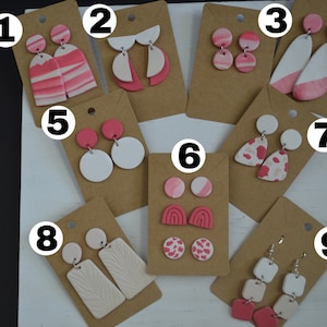 May include: Nine pairs of pink and white clay earrings displayed on brown card stock. The earrings are numbered 1 through 9.