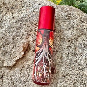 May include: A red roller bottle with a label featuring a white tree with roots and flames. The tree is surrounded by yellow and orange leaves.