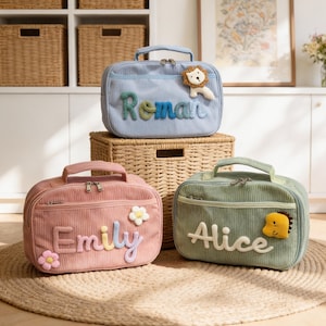 Könnte beinhalten: Drei Lunch-Taschen aus Cord in Pastellfarben: Hellblau, Rosa und Grün. Jede Tasche hat einen gestickten Namen auf der Vorderseite: "Roman", "Emily" und "Alice". Die Taschen haben dekorative Applikationen eines Löwen, Blumen und eines Dinosauriers.