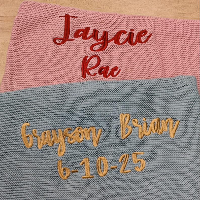 Pode incluir: Duas mantas de malha, uma rosa e outra azul. A manta rosa tem os nomes "Jaycie Rae" bordados em vermelho. A manta azul tem "Grayson Brian" e a data "6-10-25" bordados em dourado.