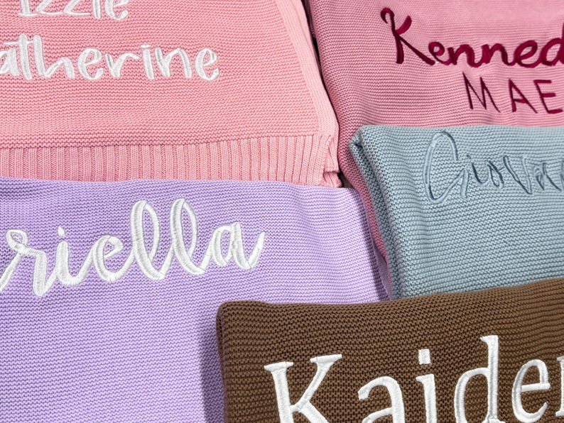 Pode incluir: Close-up de v&aacute;rias mantas de malha em v&aacute;rias cores pastel, incluindo rosa, lavanda e azul. Cada manta apresenta um nome bordado em uma cor contrastante. Os nomes est&atilde;o em uma fonte cursiva, adicionando um toque personalizado.