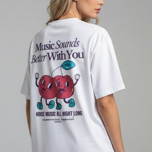 Könnte beinhalten: Ein weißes Kurzarm-T-Shirt mit einer Grafik auf der Rückseite, die zwei rote Cartoon-Kirschen mit Armen und Beinen zeigt. Der Text lautet Music Sounds Better With You, HOUSE MUSIC ALL NIGHT LONG und cannerie apparel mit fünf kleinen Sternen.