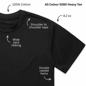 May include: A black AS Colour 5080 Heavy Tee made of 100% cotton. Features include wide neck ribbing, shoulder to shoulder tape, double needle hems, and a fabric weight of 8.2 oz. The shirt is shown with labels pointing to these specific construction details.