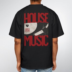 May include: Black t-shirt with a red graphic on the back that says "HOUSE MUSIC". The graphic includes a record and the words "HOUSE IS A FEELING". The shirt is a casual, oversized fit.