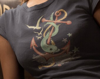 Op de afbeelding: Marineblauw T-shirt met een nautisch ontwerp. De afbeelding bevat een rode anker, een groene dolfijn, een zeemeeuw en sterren. Het ontwerp heeft een vintage, licht verweerde uitstraling.