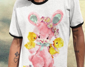May include: White ringer t-shirt with a black collar and sleeve trim. The shirt features a pink bunny graphic with yellow chicks, flowers, and a blue bow. The bunny has large ears and is holding the chicks.