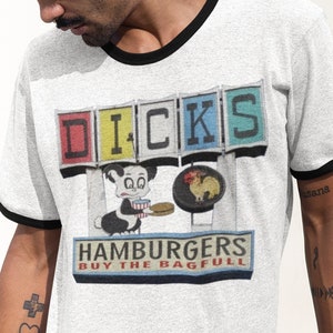 May include: A white t-shirt with a black ringer, featuring a vintage-style illustration of a restaurant sign with the text "DICK'S HAMBURGERS BUY THE BAGFULL".