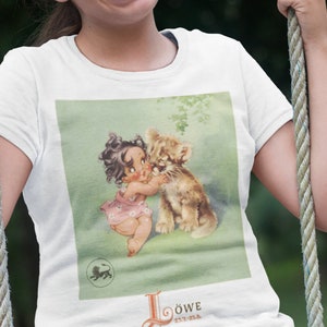 May include: A white t-shirt with a vintage illustration of a little girl hugging a lion cub. The illustration is on a green background with the text "Löwe 23.7.-22.8." at the bottom.