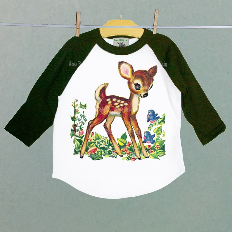 May include: White, green, and brown baseball tee shirt with a vintage illustration of a fawn with two bluebirds in a field of flowers. The text "Acme Baby Co." is printed on the shirt.
