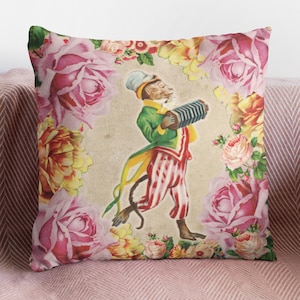 Op de afbeelding: Een decoratief kussen met een vintage illustratie van een aap die accordeon speelt, omringd door roze en gele rozen.