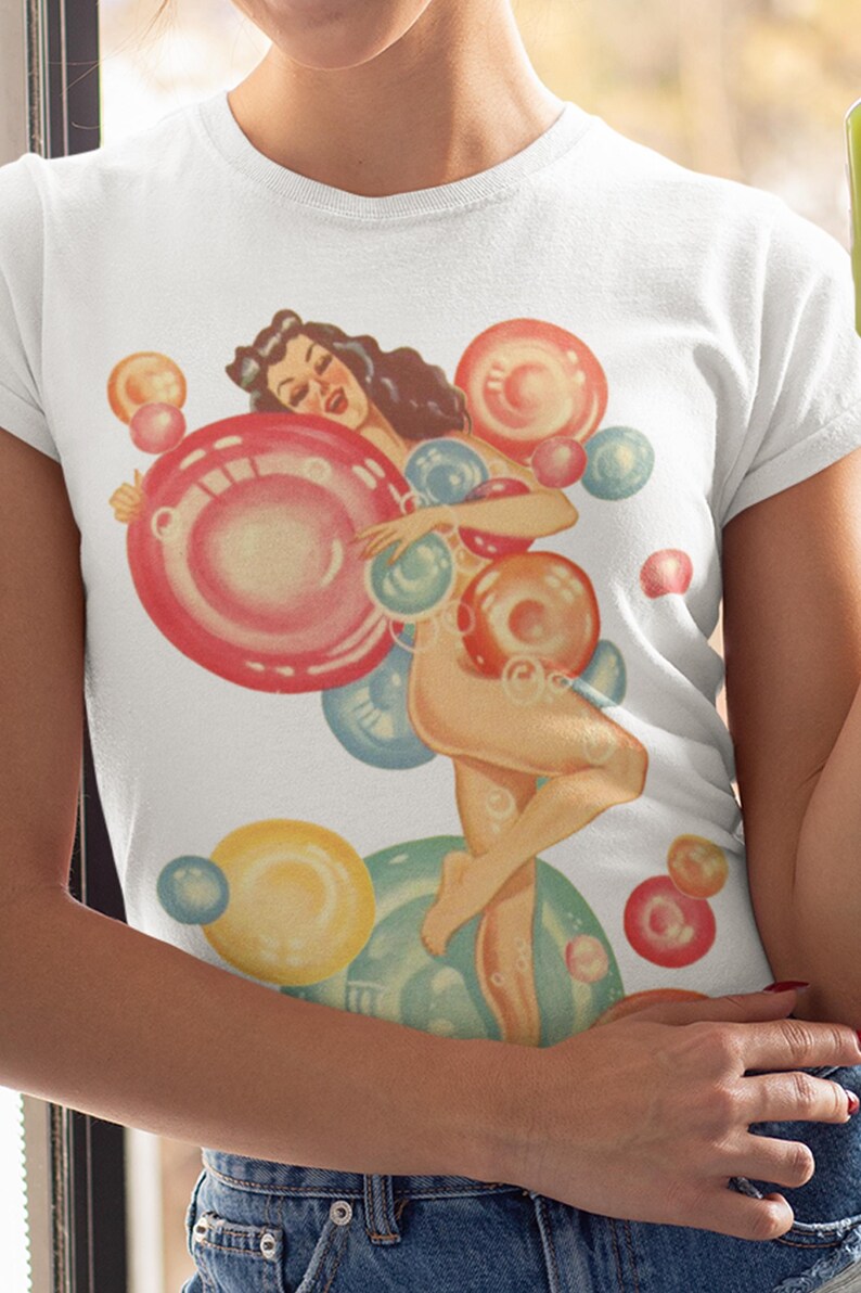 May include: A white short-sleeved t-shirt featuring a vintage-style illustration of a person with dark hair surrounded by numerous colorful, translucent bubbles in shades of red, yellow, and blue, creating a playful and vibrant graphic design.